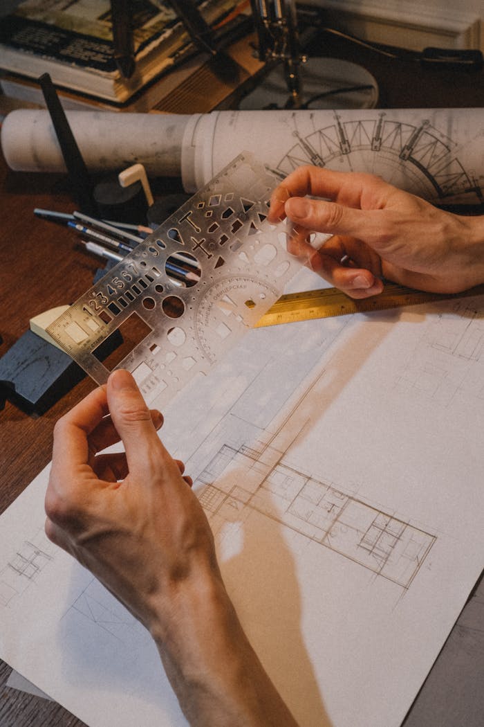 Close-up of hands using a stencil for architectural drawing, indoors on a wooden desk.
