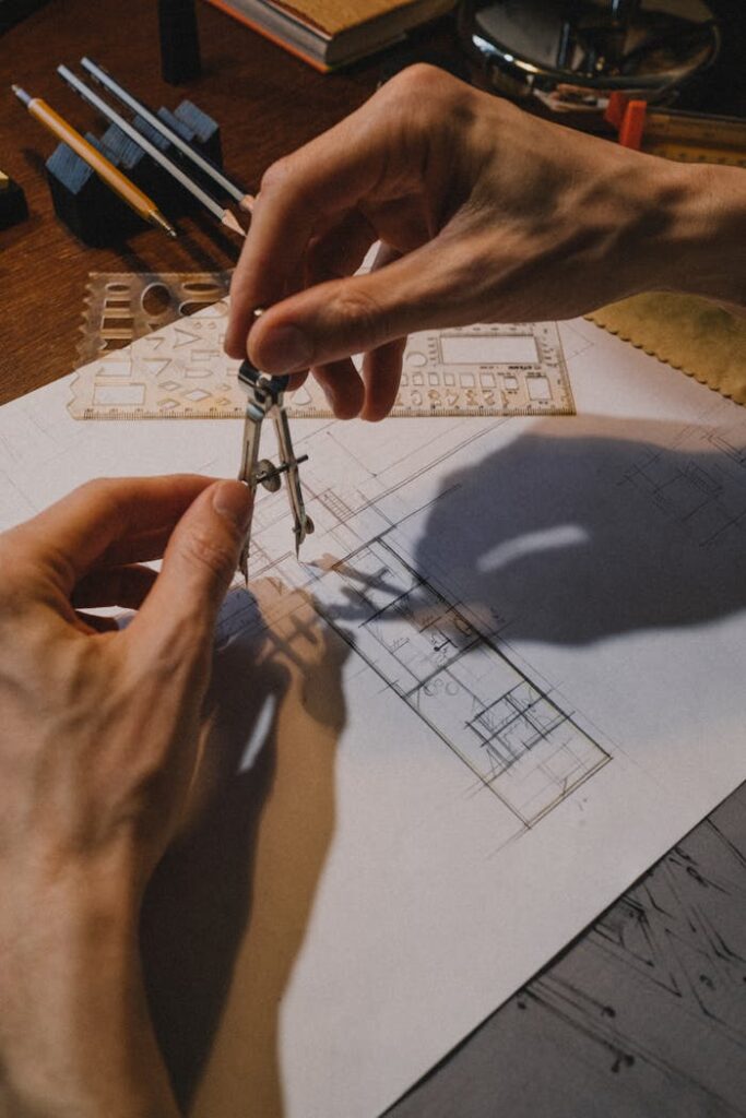 Detailed shot of hands using a compass on an architectural blueprint with drafting tools.